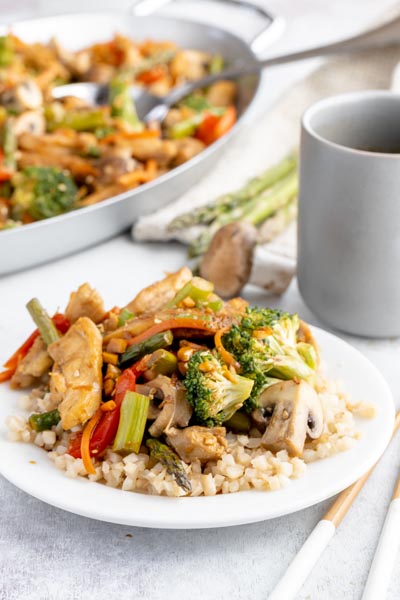 stir fry over a bed of white cauliflower rice in front of a gray pitcher and a skillet with more stir fry