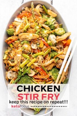 looking down on an oval skillet pan with mushrooms, asparagus and broccoli mixed with chicken and topped with sesame seeds