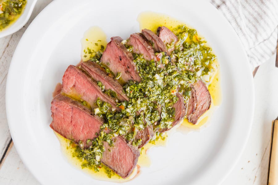 several slices of medium rare steak covered with a green chimichurri sauce