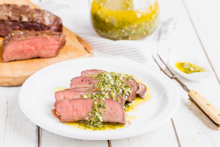 herb chimichurri sauce over sliced steak with medium rare steak in the background
