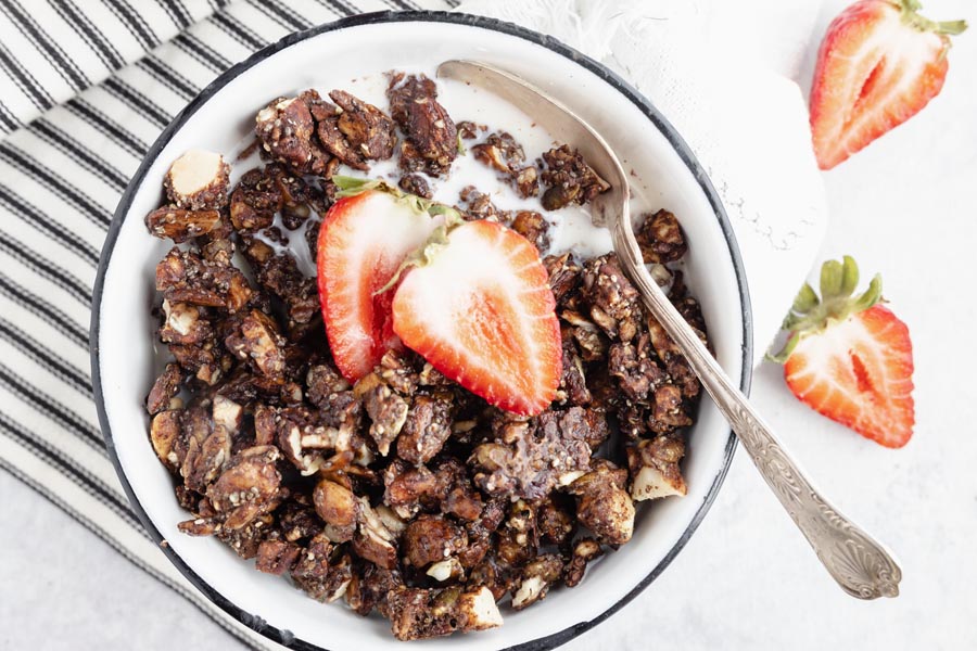 a bowl of chocolate granola with a spoon in the milk and sliced strawberries near