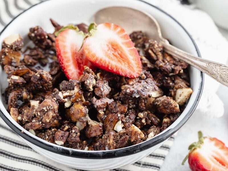 crunchy chocolate granola in a white bowl with strawberries on top
