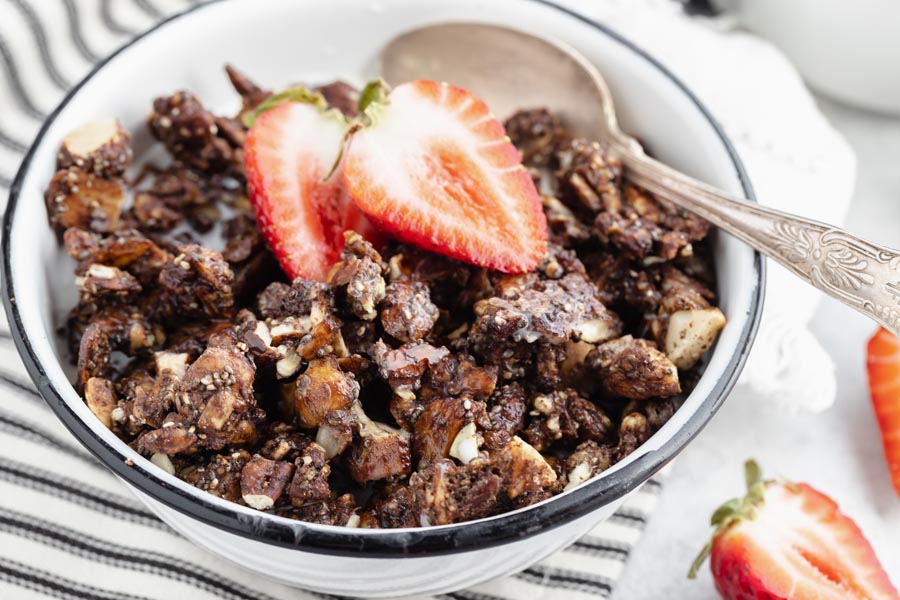 crunchy chocolate granola in a white bowl with strawberries on top