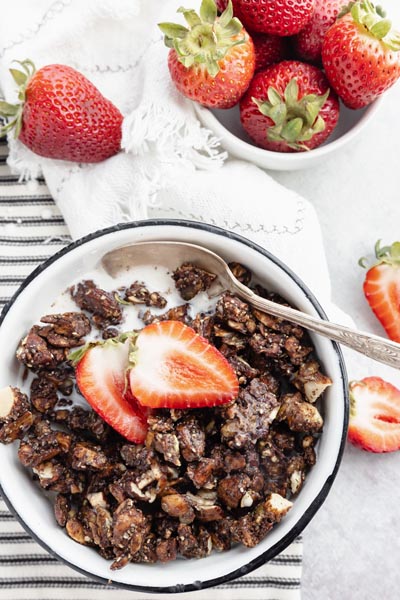 a bowl of strawberries sits next to a bowl of cereal and milk