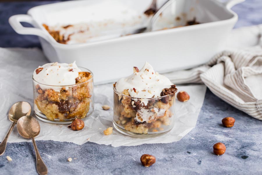 whipped topping on a couple of small dishes of warm cake with hazelnuts around and spoons