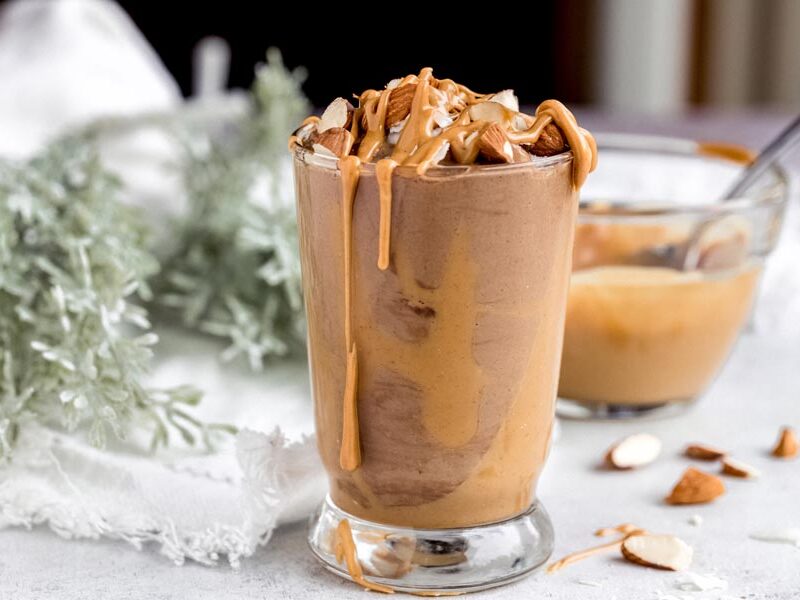 peanut butter chocolate smoothie with peanut butter on the sides and topped with nuts