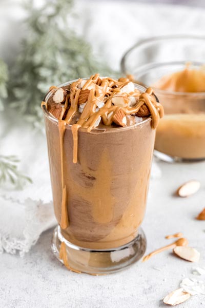 a glass with a chocolate smoothie inside peanut butter spattered around with chopped nuts on top