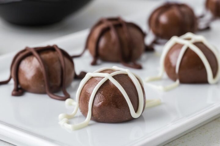 Chocolate protein balls drizzled with white and dark chocolate on a white rectangular plate.
