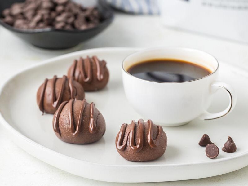 Chocolate protein balls with chocolate drizzle served alongside a cup of black coffee.