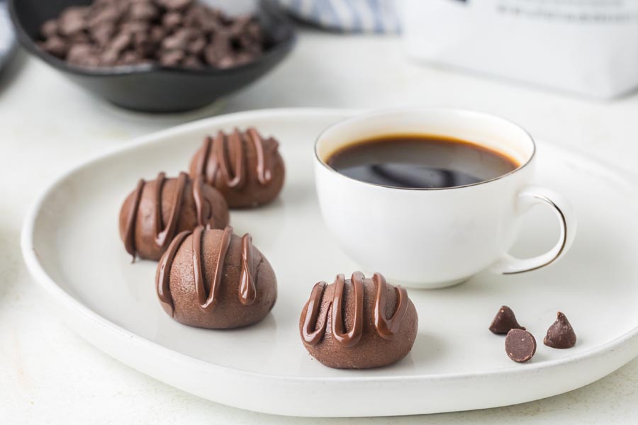 Chocolate protein balls with chocolate drizzle served alongside a cup of black coffee.