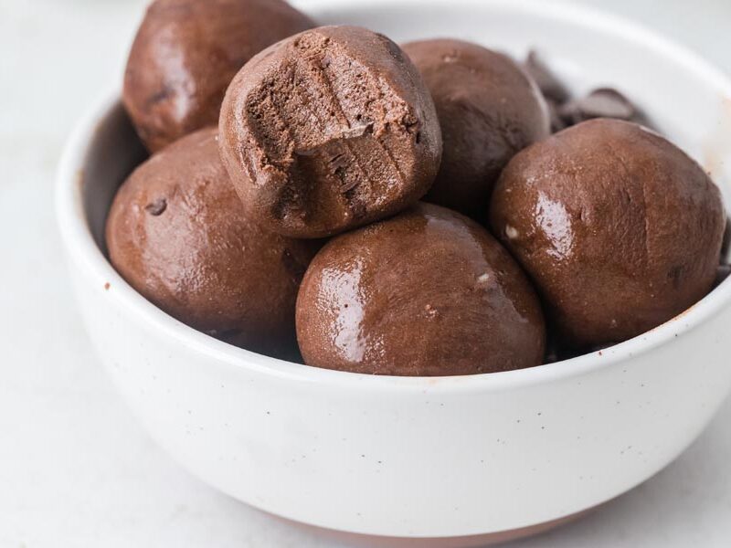 A white bowl filled with chocolate protein balls, with one ball showing a bite taken out.