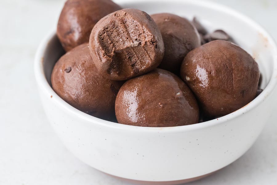 A white bowl filled with chocolate protein balls, with one ball showing a bite taken out.