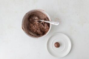 Chocolate protein dough with one ball rolled on a small plate next to the bowl.