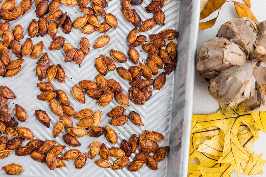 roasted pumpkin seeds on a baking tray next to leaves and a wooden pumpkin