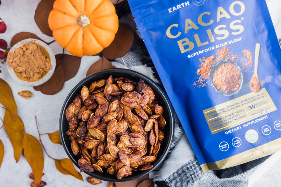 a bowl of pumpkin seeds next to a bag of cacao bliss and leaves around