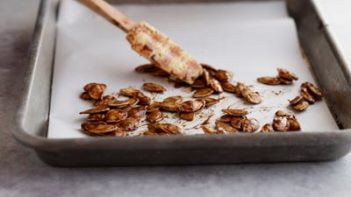 spreading pumpkin seeds on a baking tray with a spatula