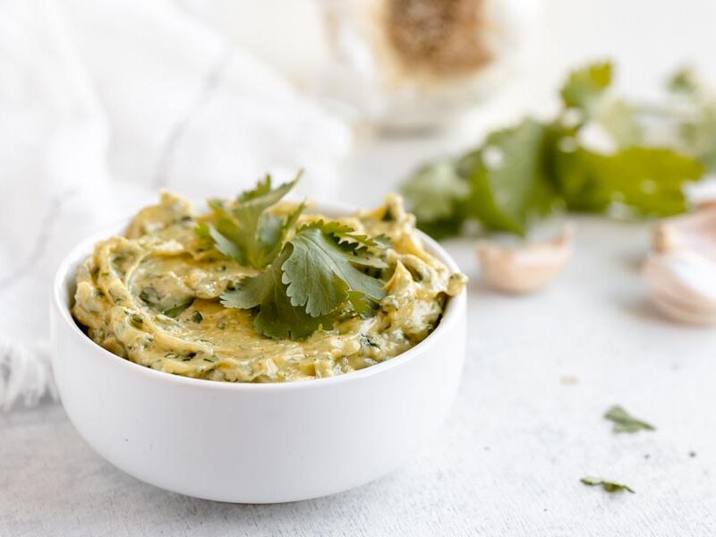 A bowl of cilantro aioli in front of garlic cloves and cilantro.