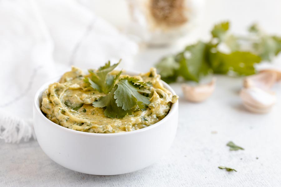 A bowl of cilantro aioli in front of garlic cloves and cilantro.