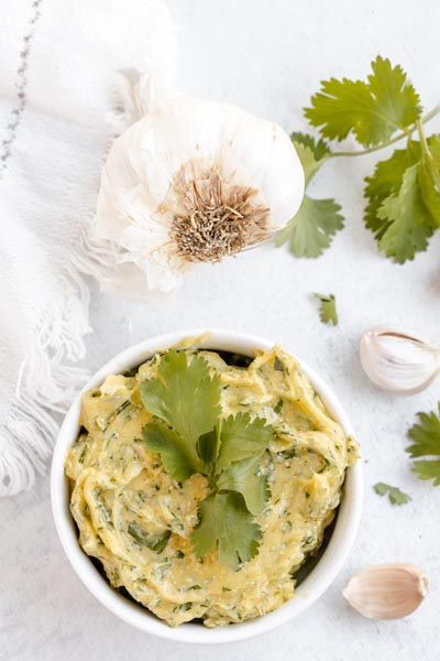 Looking down onto a small of aioli filled with cilantro leaves and a whole garlic bulb in front.