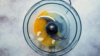 A food processor with an egg yolk and garlic cloves inside.