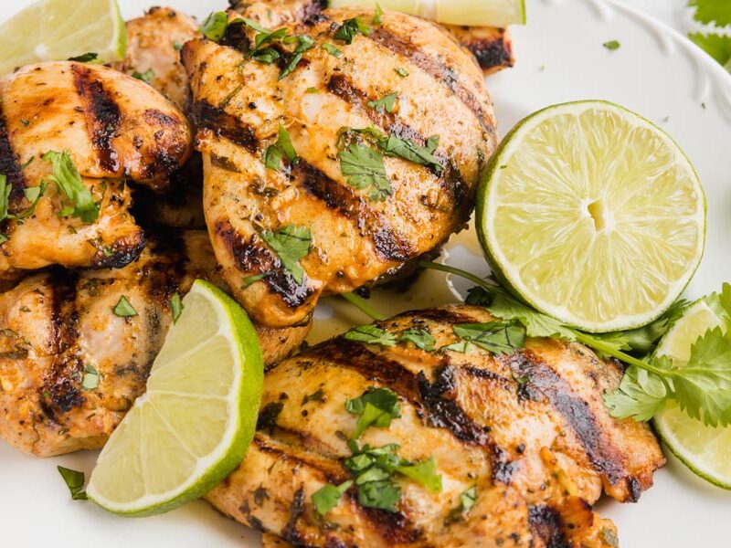 A pile of grilled cilantro lime chicken on a plate with lime edges.
