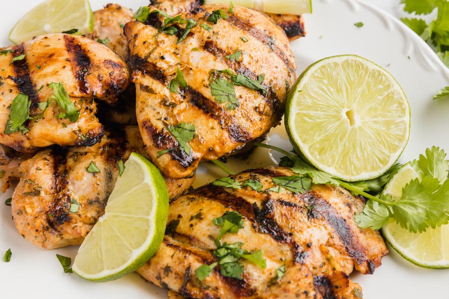 A pile of grilled cilantro lime chicken on a plate with lime edges.