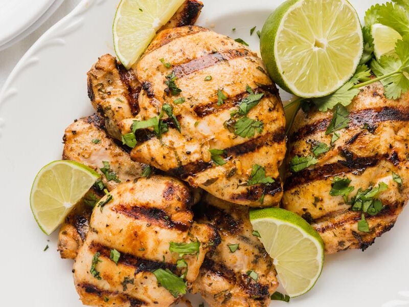 A plate with juicy grilled chicken on it covered in cilantro and limes.