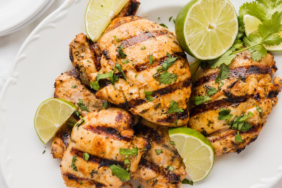 A plate with juicy grilled chicken on it covered in cilantro and limes.