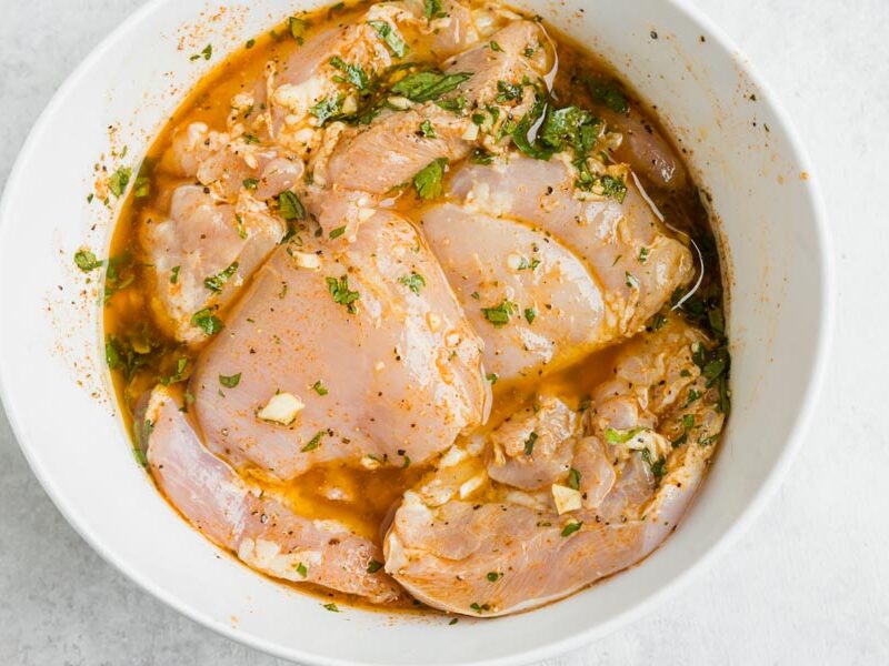 A bowl of raw chicken thighs soaking in a marinade.