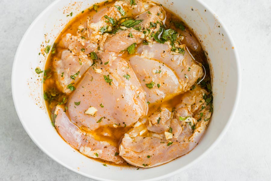 A bowl of raw chicken thighs soaking in a marinade.
