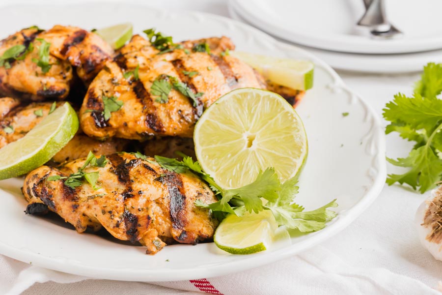 A platter with juicy chicken with cilantro sprinkled on top and limes arounds.