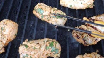 Chicken thighs on a grill with thongs turning one piece.