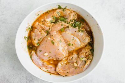 Looking into a white bowl filled with chicken marinating in a cilantro lime sauce.