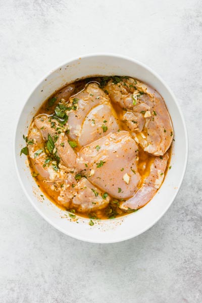 A bowl of thicken thighs marinating in a mixture of garlic, cilantro and other ingredients.