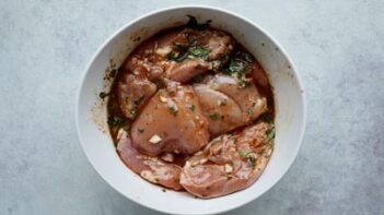 Chicken thighs marinating in a white bowl.