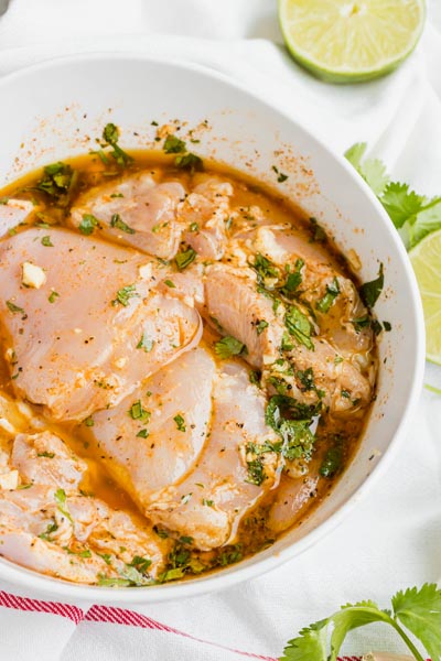 Looking into a bowl filled with raw chicken soaking in a marinade with flakes of cilantro around.