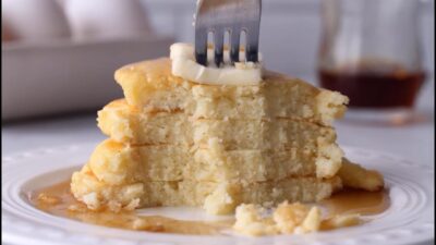 Fork cutting into a stack of cottage cheese pancakes topped with butter and syrup.