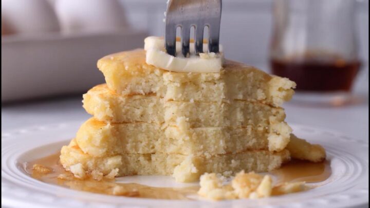 A fork cutting into a stack of fluffy cottage cheese pancakes topped with butter and sugar-free maple syrup.