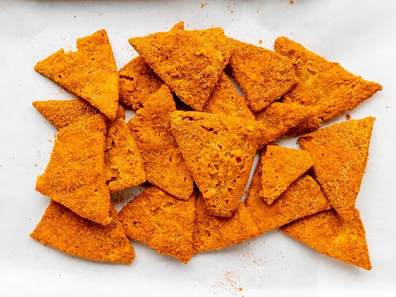 Overhead view of a pile of homemade cottage cheese chips spread across parchment paper.