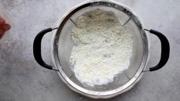 Cottage cheese being strained through a fine mesh sieve to remove excess moisture before baking.