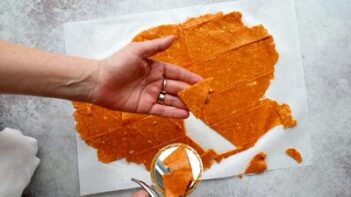 A hand lifting a cut triangle from a thin sheet of baked cottage cheese chip dough.