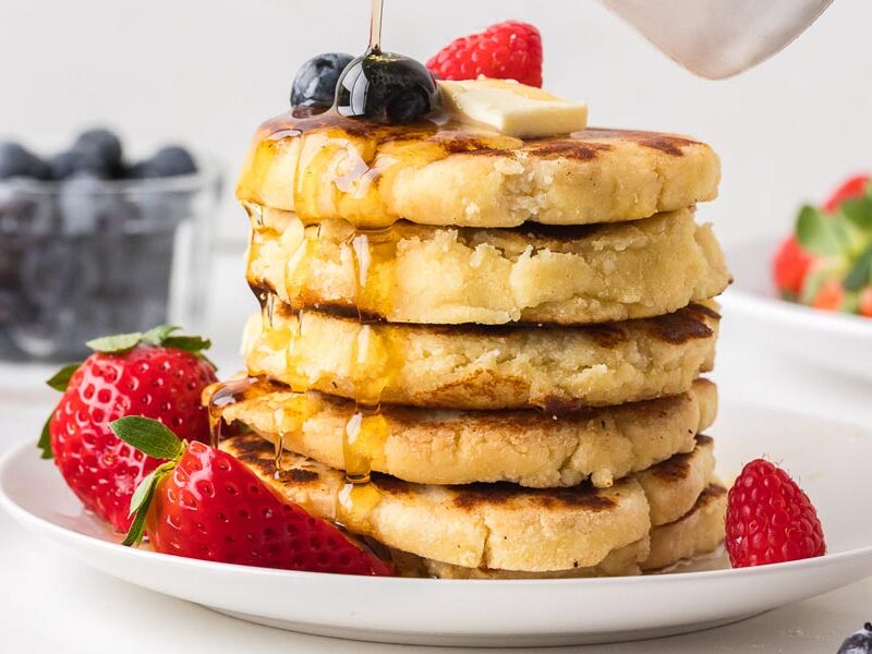 Stack of cottage cheese pancakes with butter, berries and syrup.