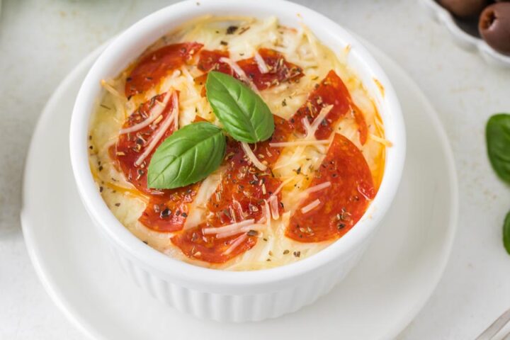 A mini pizza in a ramekin topped with pepperoni, basil and parmesan cheese.