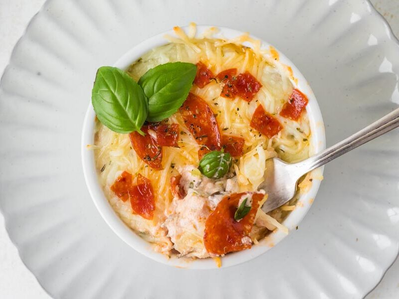 A fork digging into a cottage cheese pizza bowl topped with pepperoni.