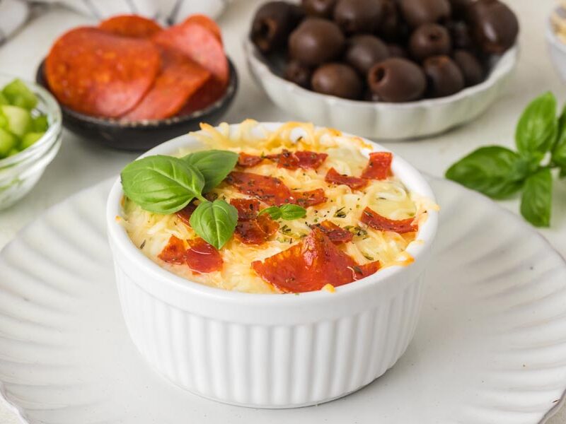 A baked cottage cheese bowl topped with pepperoni with other pizza toppings in the background.