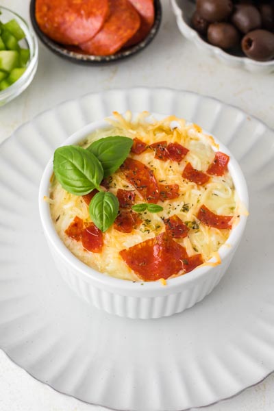 Baked pizza bowl in a ramekin on a plate and topped with fresh basil.
