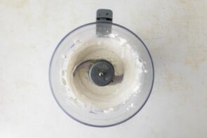 A food processor with blended cottage cheese inside.