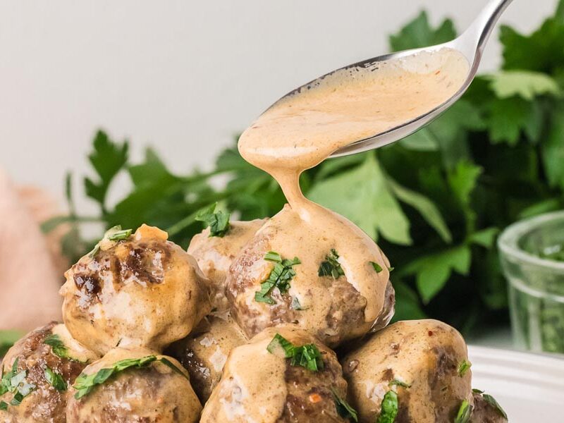A spoon drizzling creamy cowboy butter sauce over juicy beef meatballs topped with fresh chopped parsley.