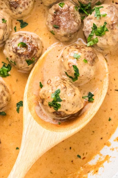 Two cowboy butter meatballs resting in a wooden spoon surrounded by a rich, creamy garlic butter sauce and fresh parsley.