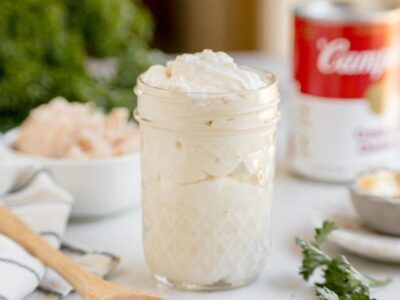 Homemade keto cream of chicken soup with a thick, creamy texture served in a glass jar with chicken and herbs in the background.